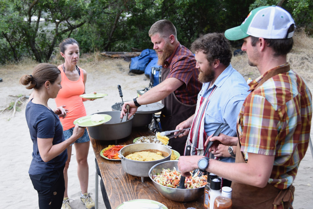 Guides serve grilled chicken and veggies, cornbread, and coleslaw during a Hells Canyon Rafting Trip's dinner