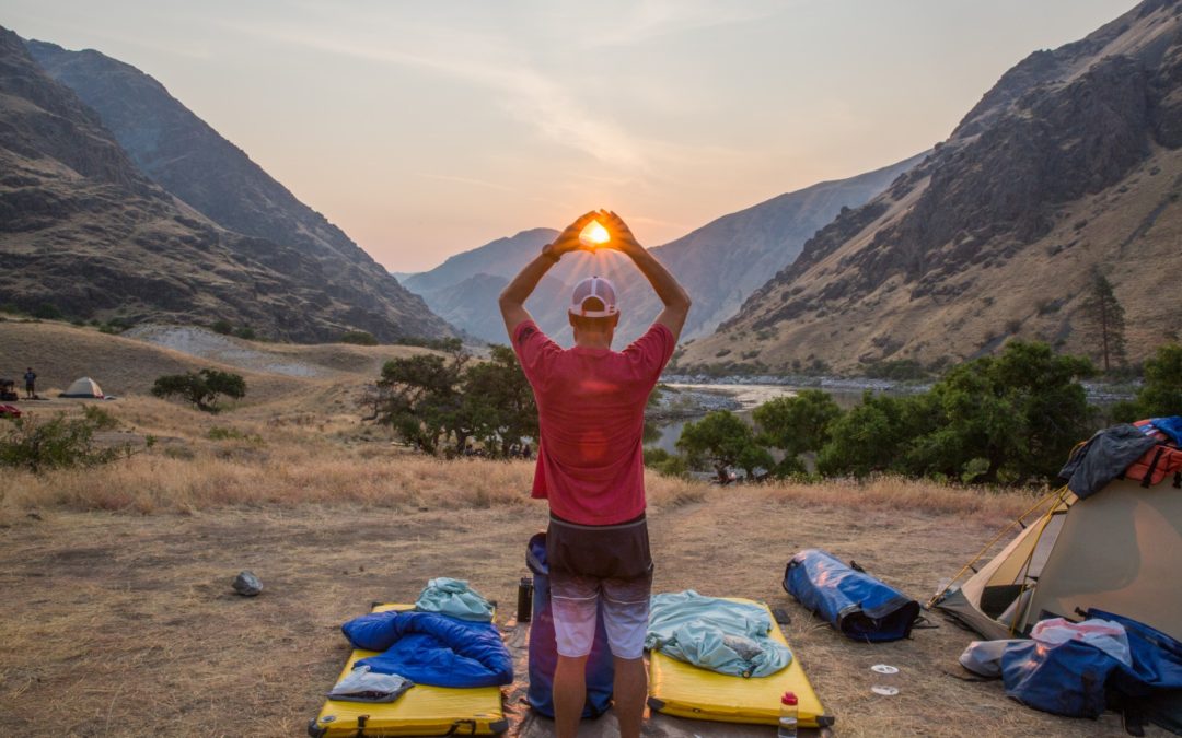 summer sun rises in hells canyon behind man holding his hands up to frame it